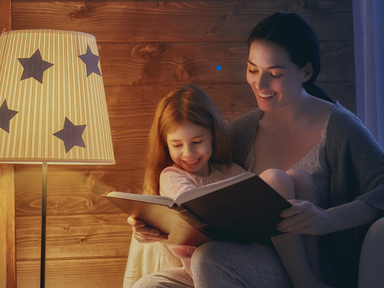 Mom holding a book and her daughter while speaking to Google Assistant